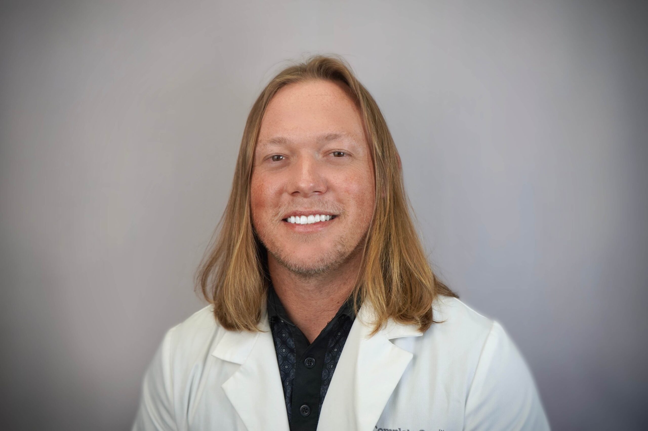 a man with long hair wearing a white lab coat that says dr.